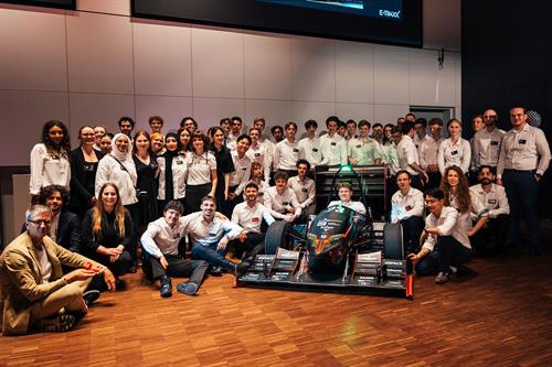 Gruppenfoto des E-Traxx-Teams der Hochschule Düsseldorf beim Rollout: Rund 50 Studierende und Beteiligte posieren in einem Hörsaal um den neuen Formula-Student-Rennwagen.